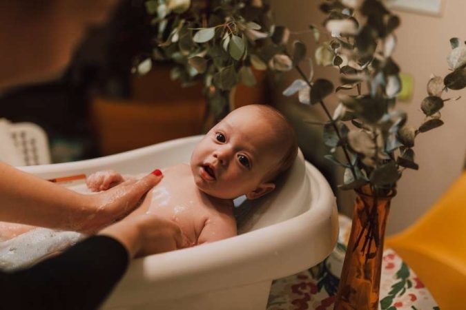 Un bébé calme profite d'un bain tiède dans une petite baignoire blanche.
