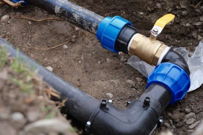 Installation de tuyaux noirs en polyéthylène avec raccords bleus enterrés dans le sol, pouvant piéger de l'air dans un réseau de plomberie.