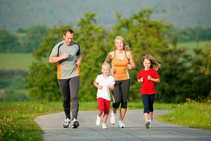 Une famille souriante court ensemble sur une route de campagne lors d'une séance d'activités à faire en famille en plein air.