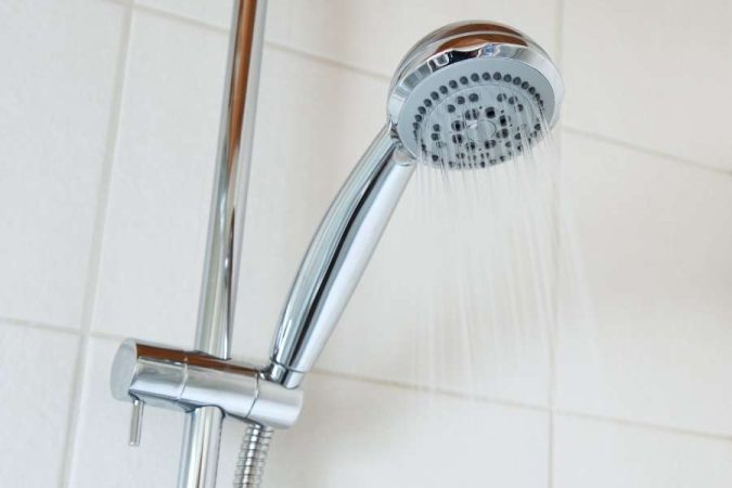 Un pommeau de douche chromé fixé sur sa barre murale laisse couler un jet d'eau dans une salle de bains.